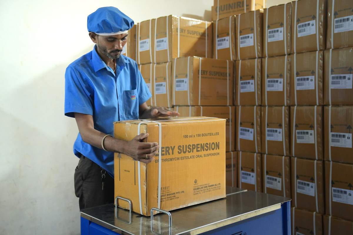 Worker strapping a shipper carton of EERY Suspension with finished cartons stacked behind