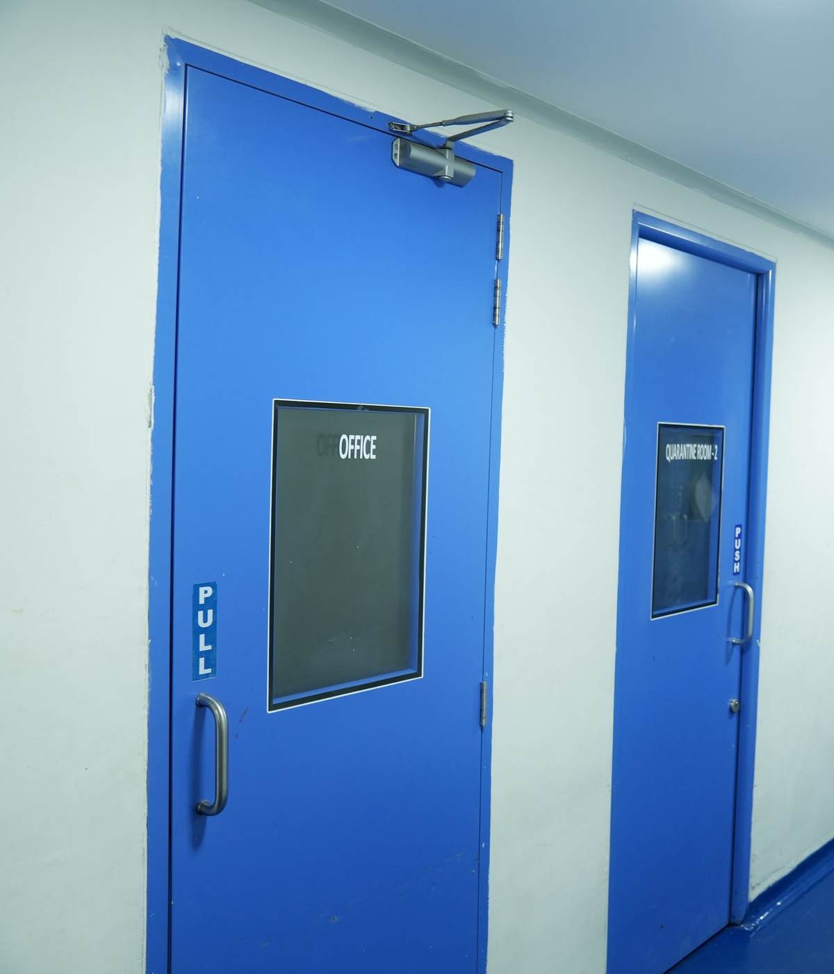 Facility corridor with blue doors to the office and quarantine room, epoxy floor and double doors at the far end